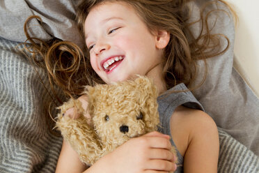 Lächelndes Mädchen hält Teddybär im Bett - CUF01102