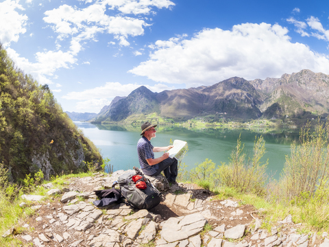 Italien, Lombardei, Quelle am Idrosee, Wanderer sitzt mit Karte am Aussichtspunkt, lizenzfreies Stockfoto