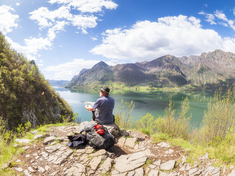 Italien, Lombardei, Quelle am Idrosee, Wanderer sitzt mit Karte am Aussichtspunkt, lizenzfreies Stockfoto