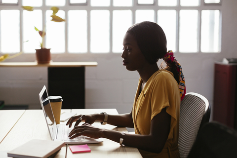 Junge Frau mit Laptop am Schreibtisch im Büro, lizenzfreies Stockfoto