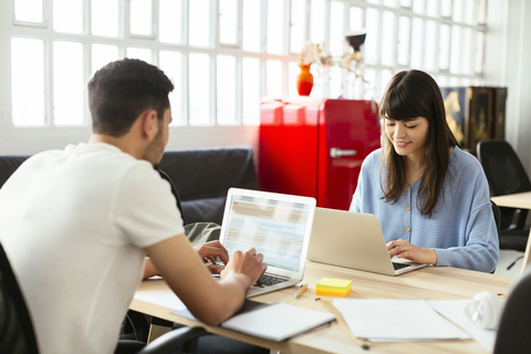 Colleagues using laptops at desk in office stock photo