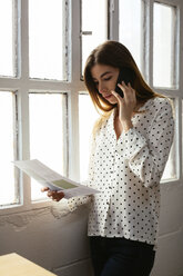 Young woman on cell phone looking at document at the window - EBSF02494