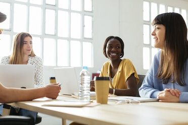 Smiling colleagues working together at desk in office - EBSF02497