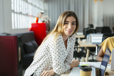 Porträt einer lächelnden jungen Frau am Schreibtisch im Büro - EBSF02507