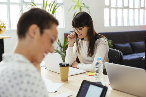 Lächelnde Kollegen bei der Arbeit am Schreibtisch im Büro - EBSF02517