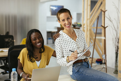 Portrait of two happy colleagues at desk in office - EBSF02522