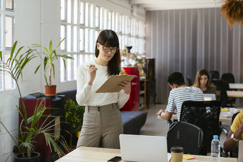 Woman with clipboard among colleagues in office - EBSF02523