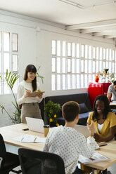 Smiling woman with clipboard among colleagues in office - EBSF02524