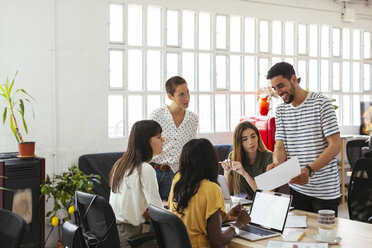 Smiling man presenting paper to colleagues at desk in office - EBSF02532