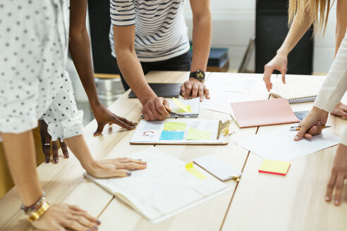 Close-up of colleagues working together at desk in office discussing papers - EBSF02538