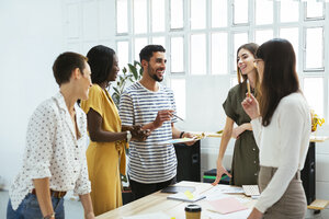 Lächelnde Kollegen arbeiten zusammen am Schreibtisch im Büro und diskutieren Papiere - EBSF02540