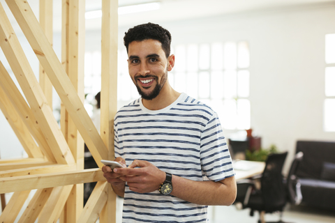 Portrait of smiling young man with cell phone in office stock photo