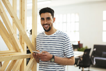 Portrait of smiling young man with cell phone in office - EBSF02545
