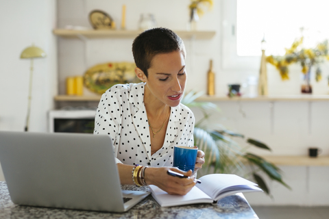 Frau trinkt Kaffee und benutzt Laptop und Notizbuch auf dem Tisch, lizenzfreies Stockfoto