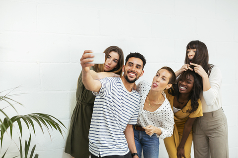 Playful colleagues standing at brick wall taking a selfie stock photo