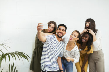 Playful colleagues standing at brick wall taking a selfie - EBSF02566