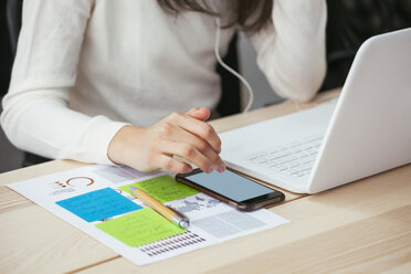 Nahaufnahme einer Frau mit Dokument, Handy und Laptop am Schreibtisch im Büro - EBSF02572