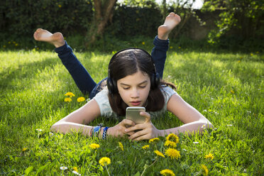 Girl lying on meadow listening music with headphones using smartphone - LVF06935