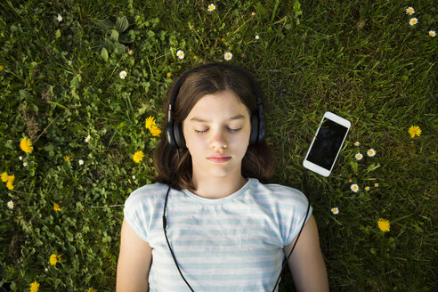Porträt eines auf einer Wiese liegenden Mädchens, das mit Kopfhörern und Smartphone Musik hört - LVF06939