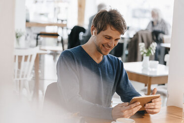 Smiling man in a cafe with earphone using tablet - KNSF03837