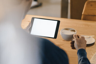 Close-up of man in a cafe holding tablet and drinking coffee - KNSF03840