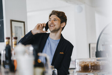 Lächelnder Mann in einem Café, der mit seinem Handy telefoniert - KNSF03850