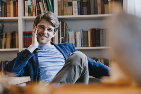 Porträt eines lächelnden Mannes, der an einem Bücherregal sitzt, lizenzfreies Stockfoto