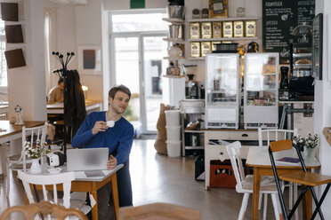 Mann sitzt am Tisch in einem Café mit Laptop - KNSF03870