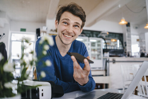 Smiling man in a cafe with cell phone and laptop - KNSF03875