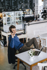 Lächelnder Mann in einem Café mit Laptop auf einem Mobiltelefon - KNSF03876