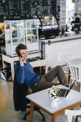 Smiling man in a cafe with laptop on cell phone - KNSF03876