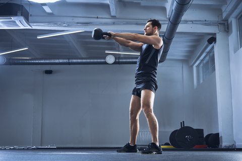 Athletischer Mann bei einer Kettlebell-Schwungübung im Fitnessstudio, lizenzfreies Stockfoto
