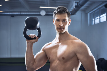 Athletischer Mann ohne Hemd posiert mit Kettlebell im Fitnessstudio - BSZF00325