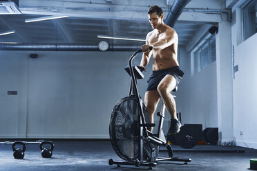 Athletic man doing HIIT workout on airbike at gym - BSZF00328