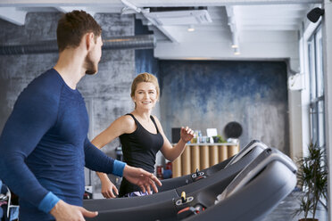 Mann und Frau unterhalten sich während des Trainings auf dem Laufband im Fitnessstudio - BSZF00329