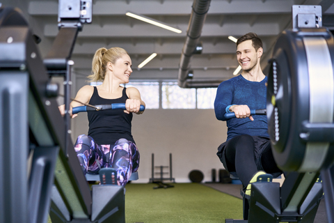 Man and woman at gym exercising together on rowing machines stock photo