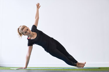 Woman doing side plank yoga exercise in studio - BSZF00345