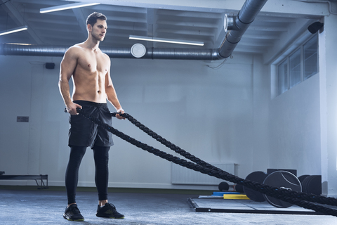 Athletischer Mann beim Training mit Kampfseilen im Fitnessstudio, lizenzfreies Stockfoto