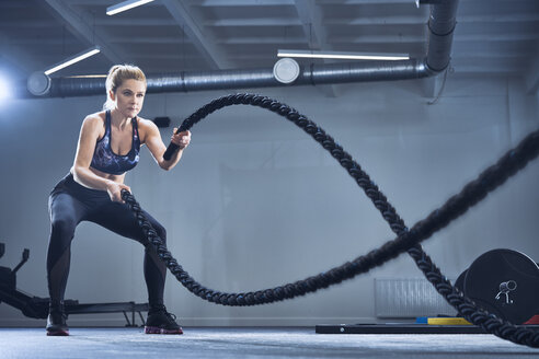 Sportliche Frau beim Training mit Kampfseilen im Fitnessstudio - BSZF00355