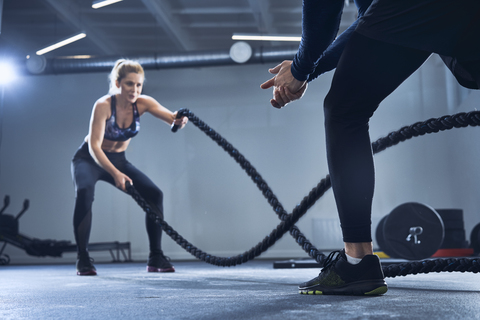 Athletic woman doing battlerope exercise with personal trainer at gym stock photo