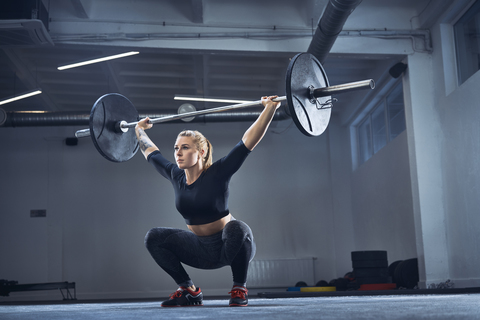 Frau macht Überkopfhocke Übung im Fitnessstudio, lizenzfreies Stockfoto