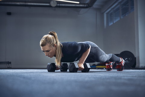 Frau beim Üben von Liegestützen mit Hanteln im Fitnessstudio, lizenzfreies Stockfoto
