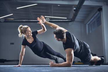 Mann und Frau machen High Five während einer seitlichen Plank-Übung im Fitnessstudio - BSZF00373