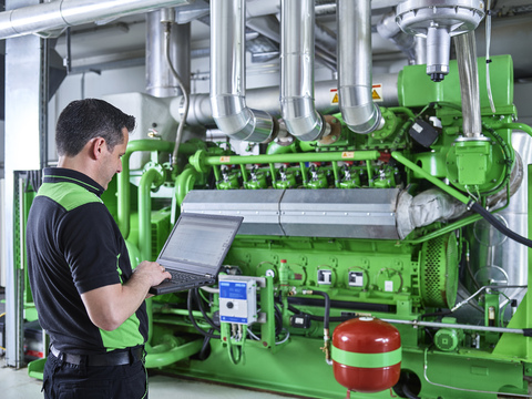 Kraft-Wärme-Kopplungsanlage, Arbeiter mit Laptop vor einem Gasmotor, lizenzfreies Stockfoto