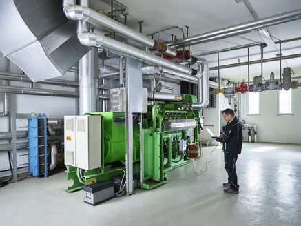 Combined heat and power plant, worker using laptop in front of gas engine - CVF00442