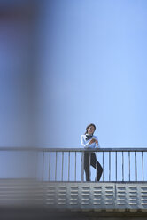 Businesswoman standing on bridge against blue sky using smartphone - BEF00027