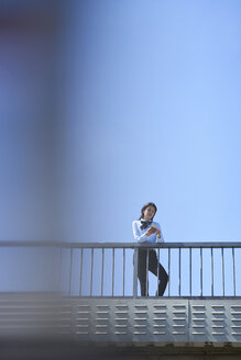 Geschäftsfrau steht auf einer Brücke vor blauem Himmel und benutzt ein Smartphone - BEF00027