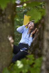 Junge Frau sitzt auf einer Wiese und hört Musik mit Kopfhörern und Mobiltelefon - BEF00033