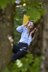 Young woman sitting on a meadow listening music with headphones and cell phone - BEF00033