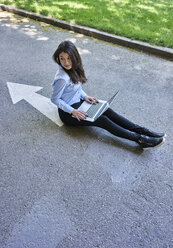 Junge Frau mit Laptop sitzt auf Pfeil Zeichen auf der Straße - BEF00036